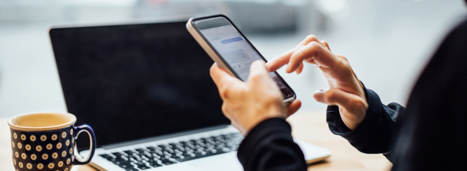 Person navigating on a mobile phone while sitting at a laptop